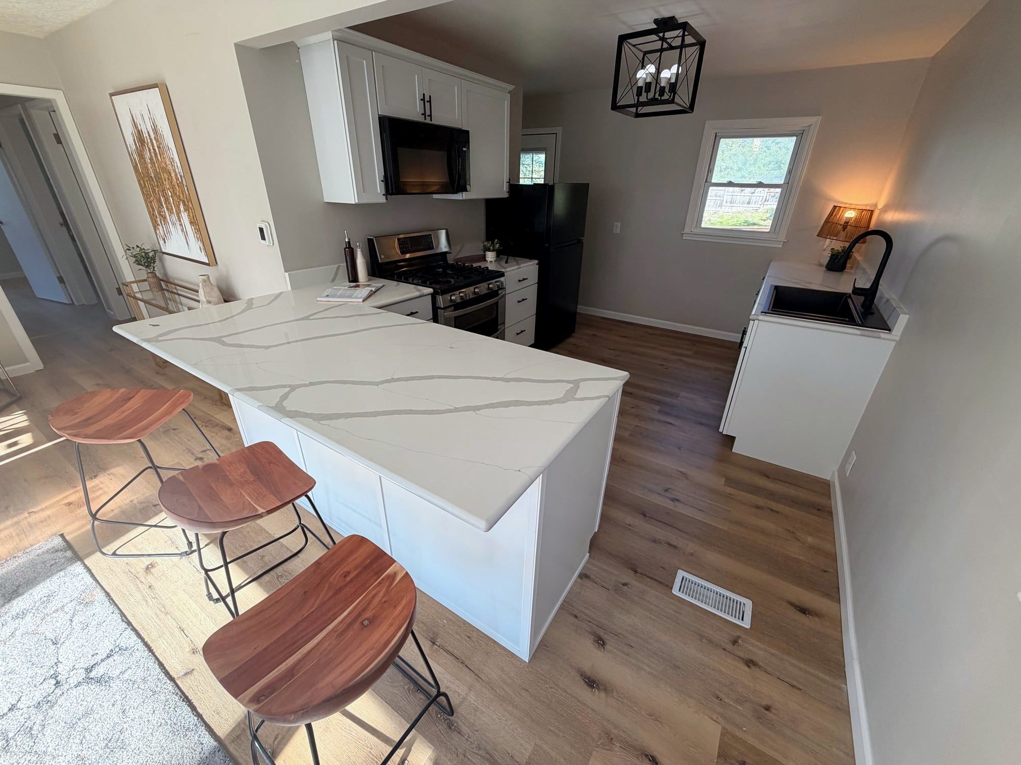 Remodeled kitchen with white cabinets and a quartz peninsula with stools